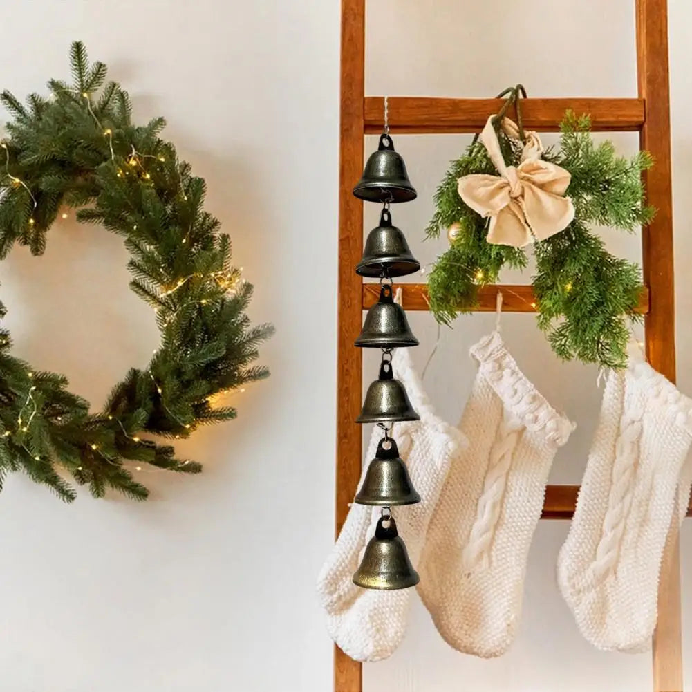 A vintage metal wind chime decoration hangs on a wooden rack, surrounded by green foliage and white fabric.