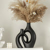 A black ceramic vase holds dried floral arrangements with feathery grasses and small yellow flowers.