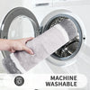 A hand is holding a gray microfiber bath mat inside a white washing machine drum.