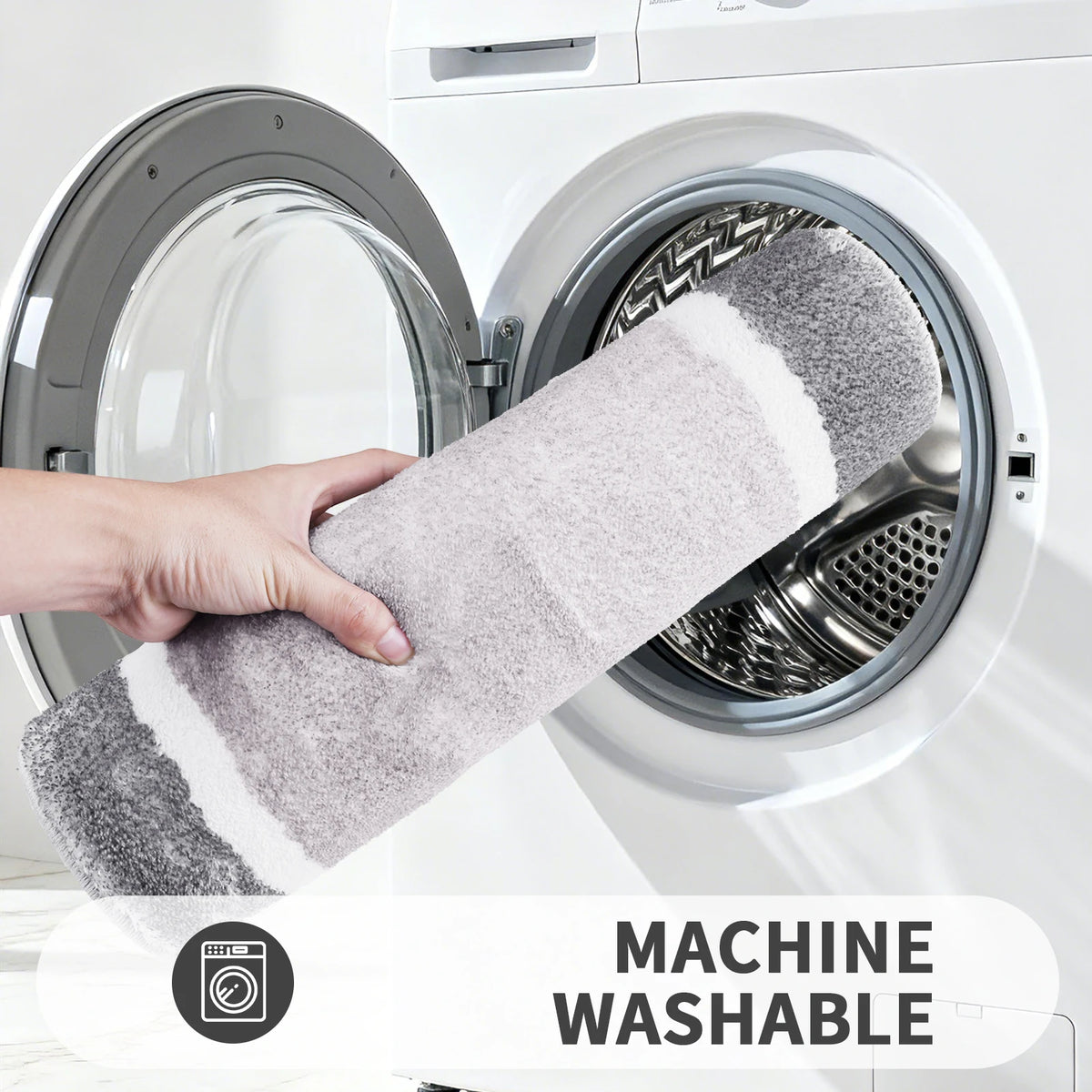 A hand is holding a gray microfiber bath mat inside a white washing machine drum.