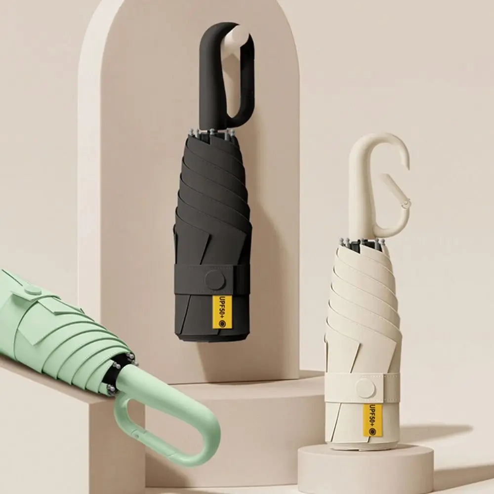 A black compact folding umbrella with a white handle is displayed against a light background.
