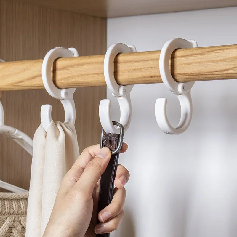 A hand is attaching a black hook to a wooden closet rod with white organizer hooks.