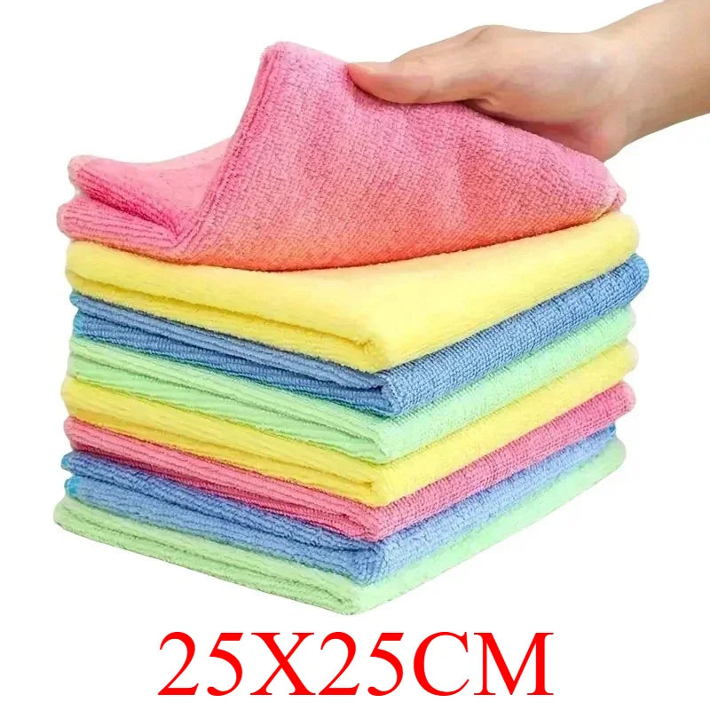 A hand is holding a stack of pink, yellow, and blue reusable microfiber cleaning cloths.