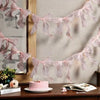 A pink decorative bowknot banner garland set displayed against a light wall with a mirror and a cake.
