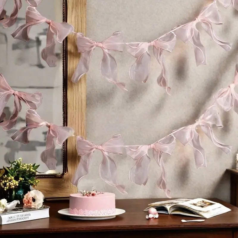 A pink decorative bowknot banner garland set displayed against a light wall with a mirror and a cake.