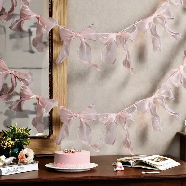 A pink decorative bowknot banner garland set displayed against a light wall with a mirror and a cake.