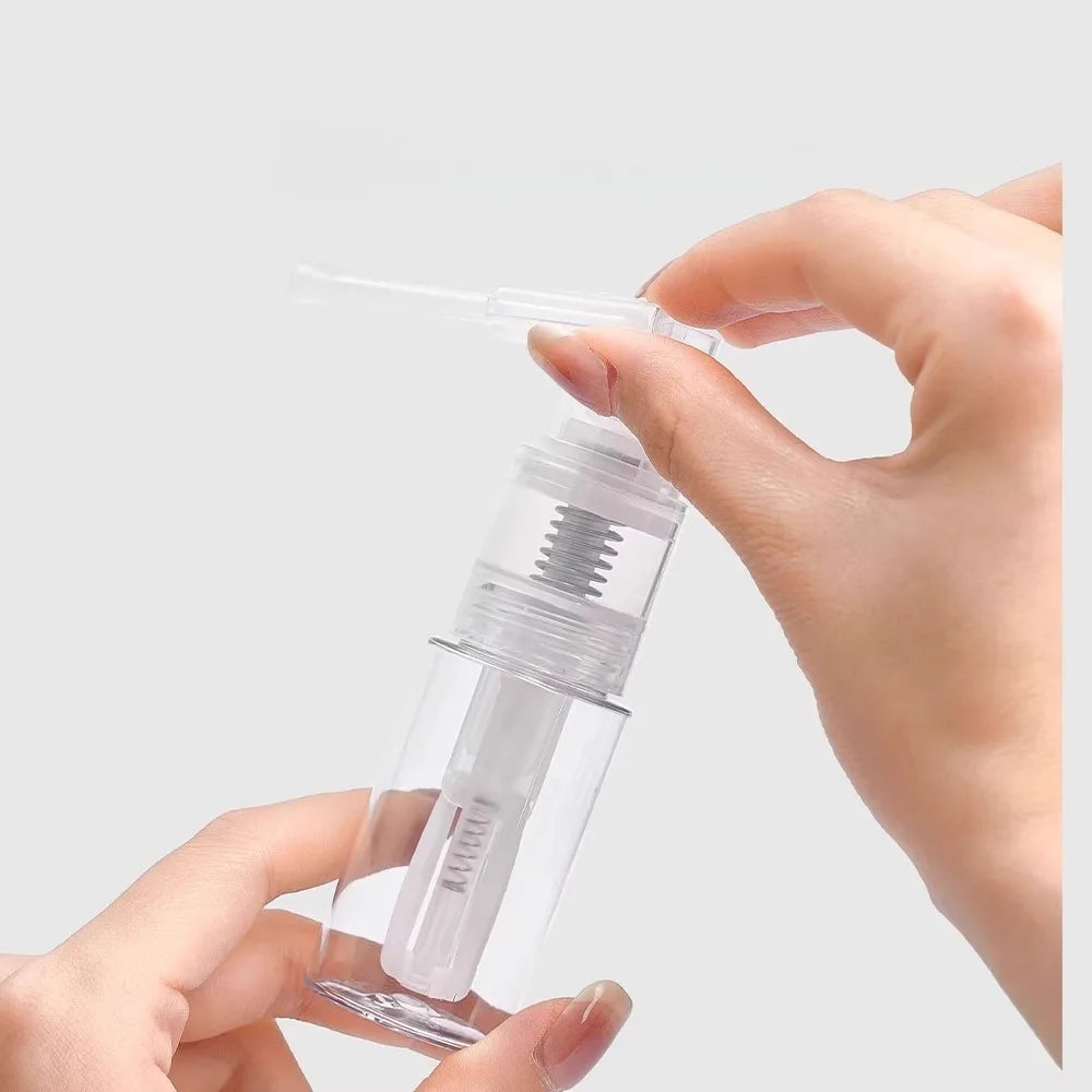 A hand is holding a clear glass bottle with a dropper and a spray nozzle, demonstrating the refillable styling mist spray bot
