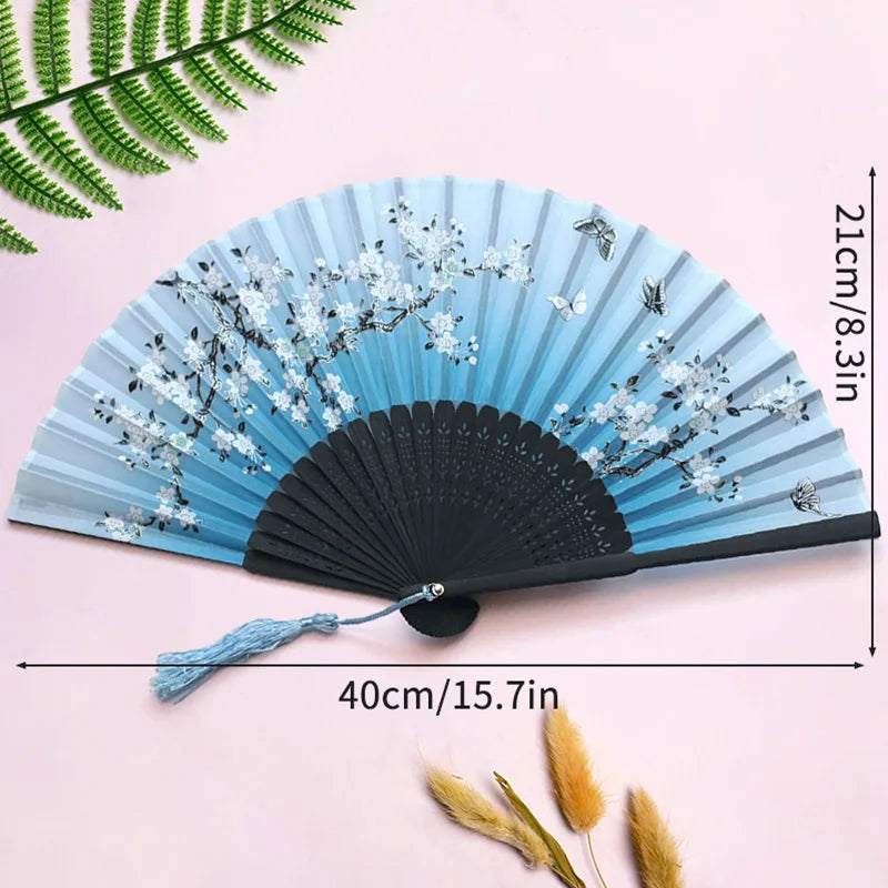 A light blue folding hand fan decorated with white and black floral patterns, shown against a pink background.