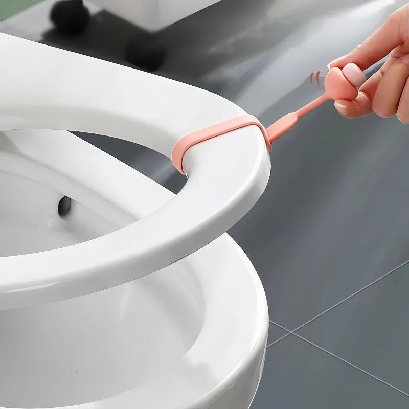 A hand is using a silicone ring opener to lift or open the lid of a white toilet seat.