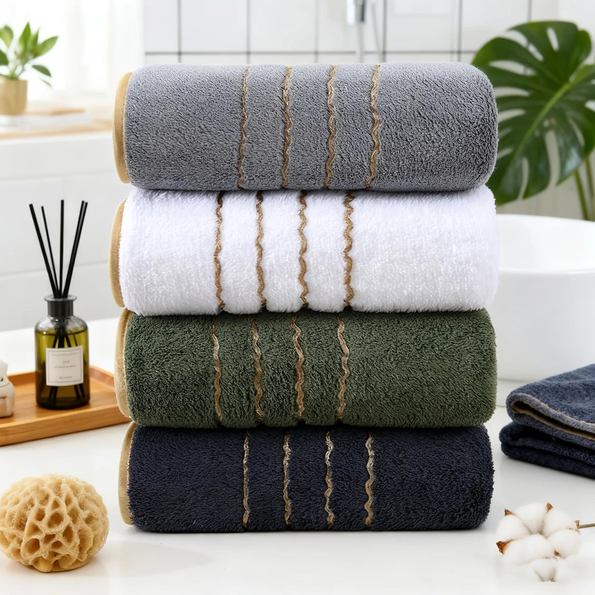A stack of coral fleece towels in various shades of gray, green, and navy blue with gold stripes.