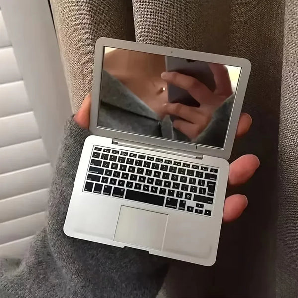 شخص يحمل مرآة مكياج محمولة وجهاز كمبيوتر صغير، منعكساً لوجهه في المرآة.