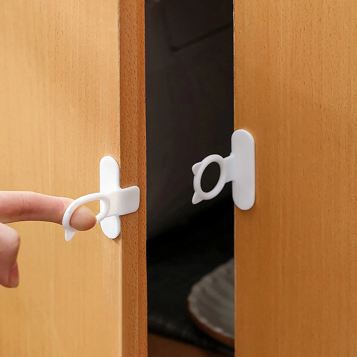 A hand is using a white silicone self-adhesive cabinet door handle lifter to open a wooden cabinet door.