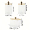 Clear glass apothecary jar with a golden lid and a separate clear plastic dispenser for cotton balls and swabs.