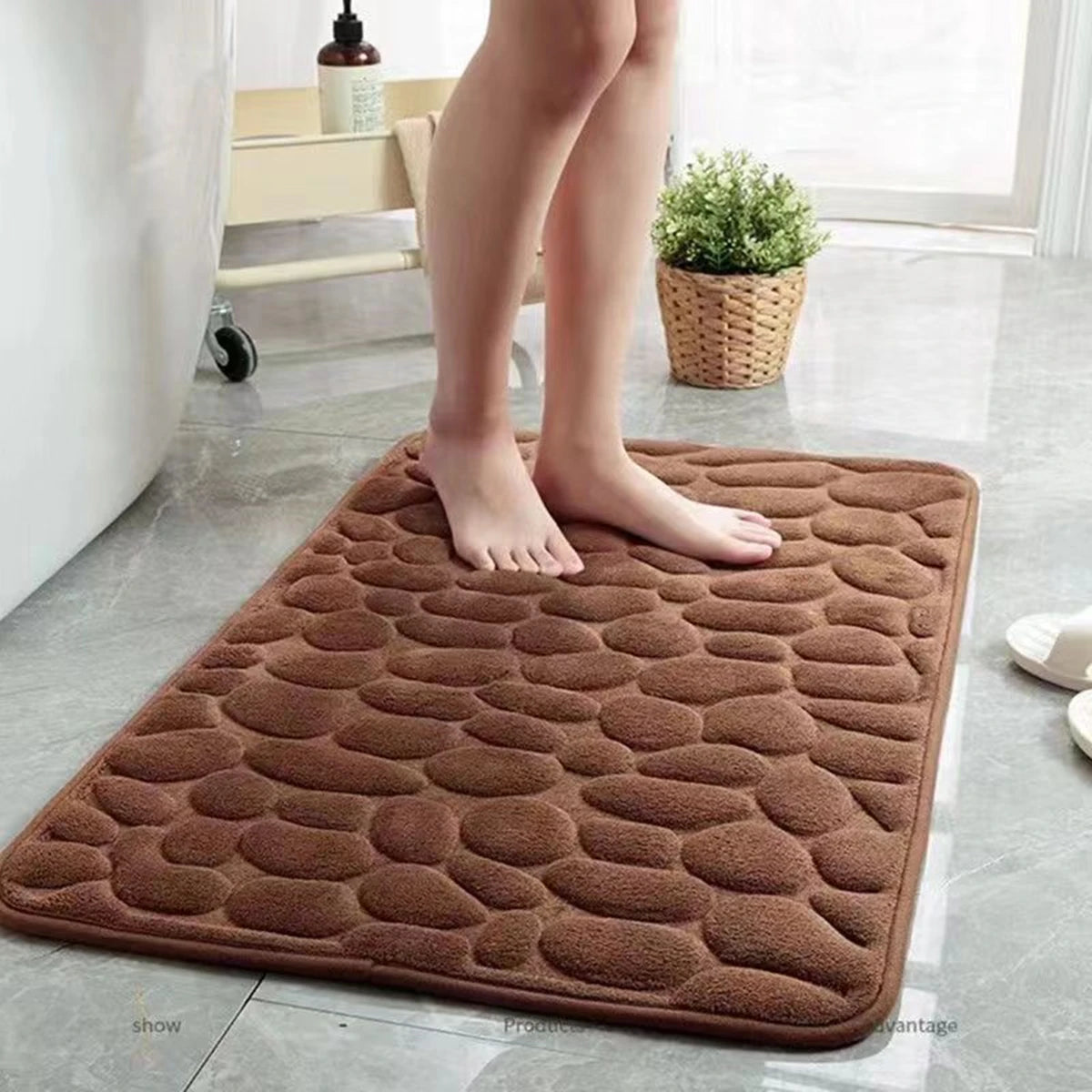 A brown, textured 3D non-slip bathroom doormat is placed on a light gray floor next to a person's legs.