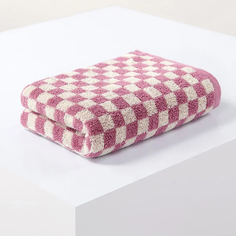 A stack of pink and cream plaid cotton bath towels folded neatly on a white surface.