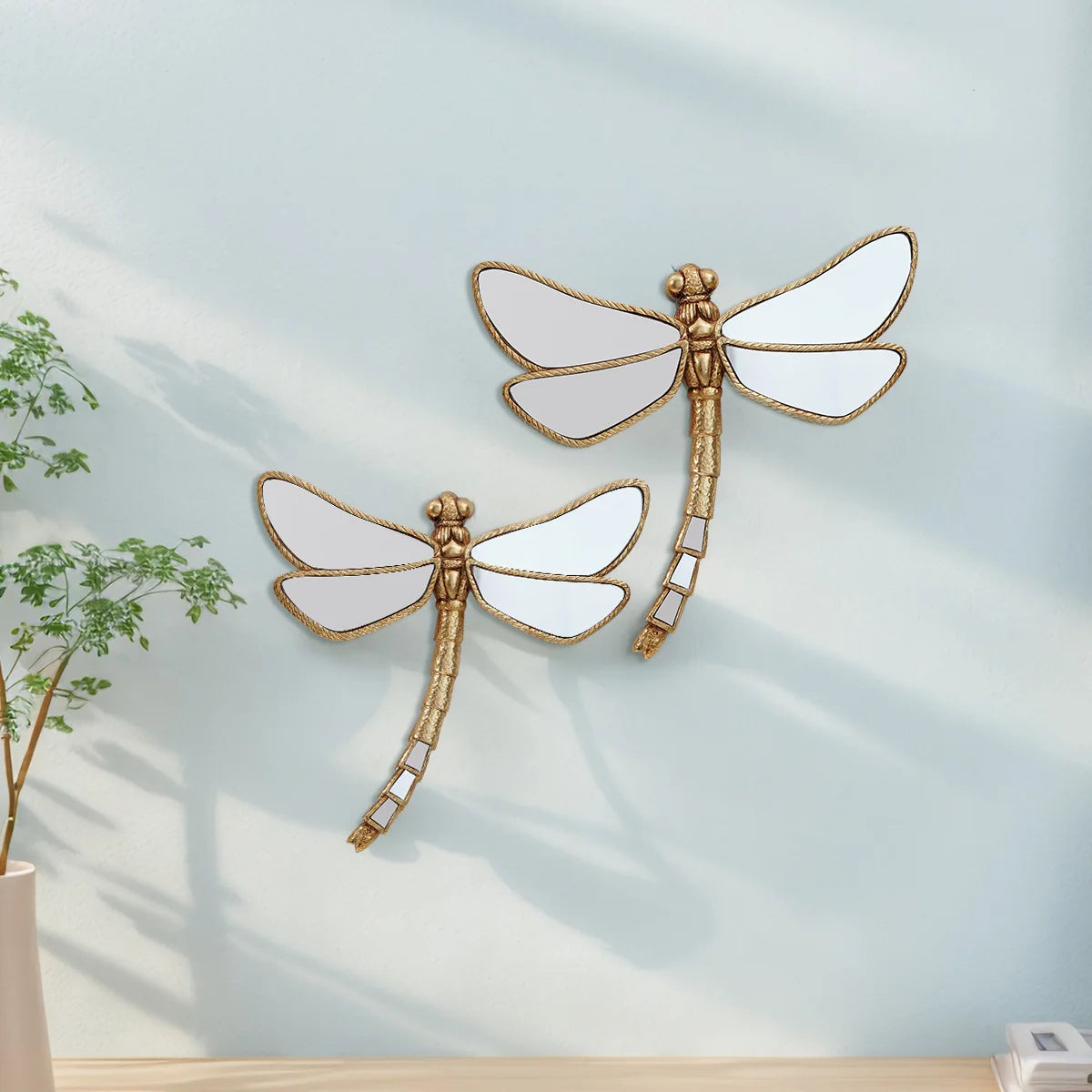 Golden dragonfly mirror wall decor featuring a detailed, gilded dragonfly design on a light blue wall.