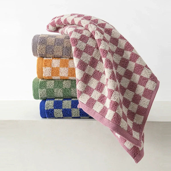 A stack of plaid cotton bath towels in various muted colors including purple, beige, green, and blue.