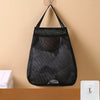 Black mesh wall mounted garbage bag storage organizer hanging on a beige wall.