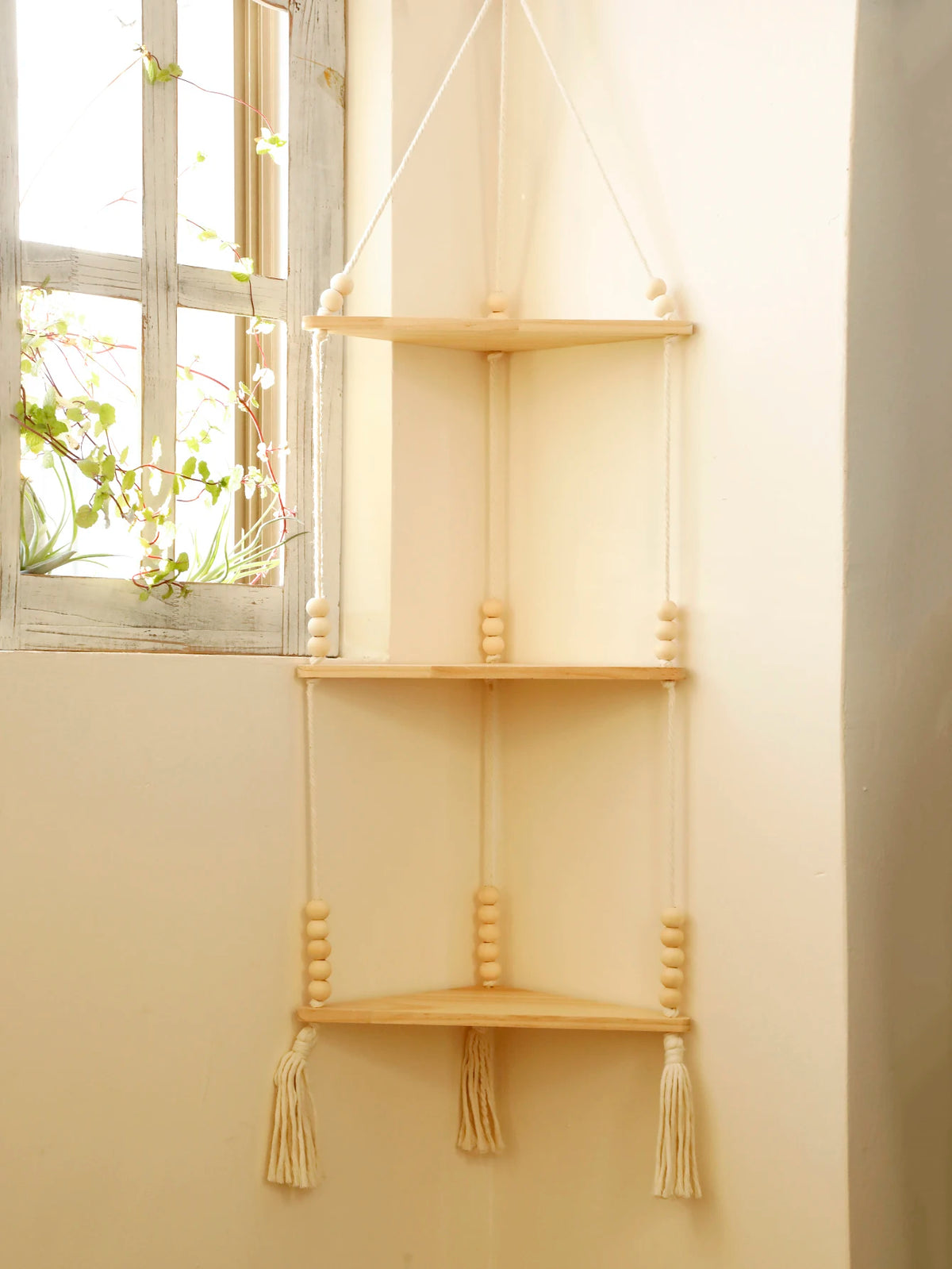 A light wood boho triangle floating wall shelf with natural twine hangers mounted on a cream-colored wall.
