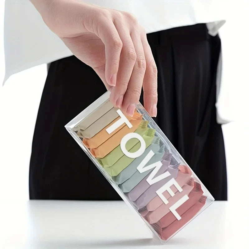 A hand is holding a clear plastic container filled with various colored disposable compressed washcloths or facial cleansing 