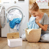 A young woman is placing a blue cloth into a woven basket next to a white dryer sheet container in front of a washing machine