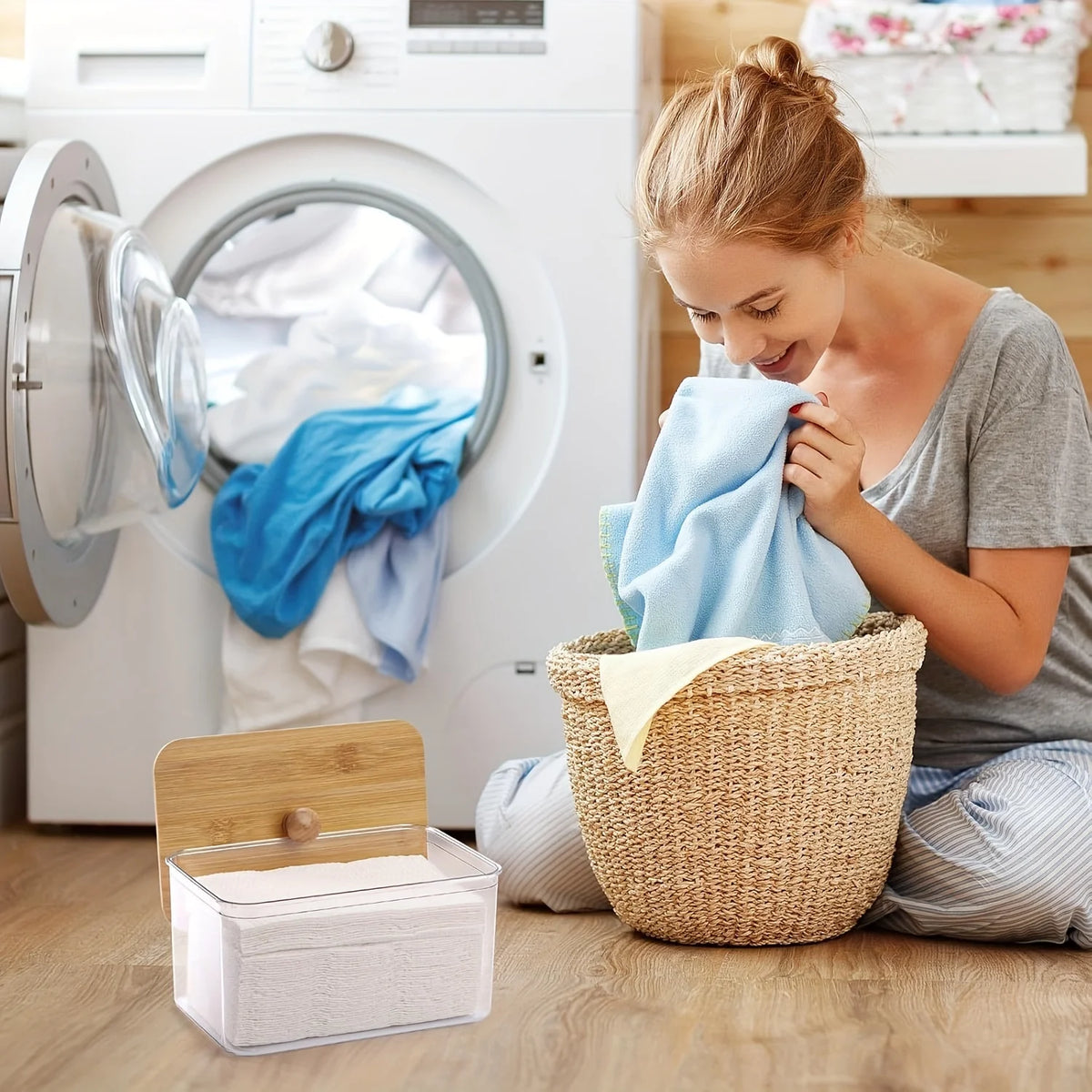 A young woman is placing a blue cloth into a woven basket next to a white dryer sheet container in front of a washing machine