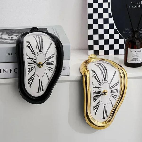 A gold-framed melting wall clock with a white face and black markings, displayed next to a dark glass bottle.