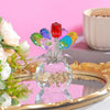 Bunte Kristallrose-Skulptur mit leuchtend pinken, blauen und gelben Blütenblättern auf einer goldgerahmten Platte.