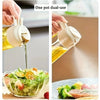 A hand is using a one pot dual-use oil spray bottle to drizzle olive oil over a fresh salad.