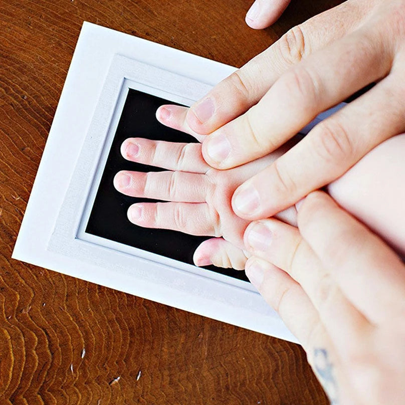 Hands print on a white frame showing baby handprints and footprints.