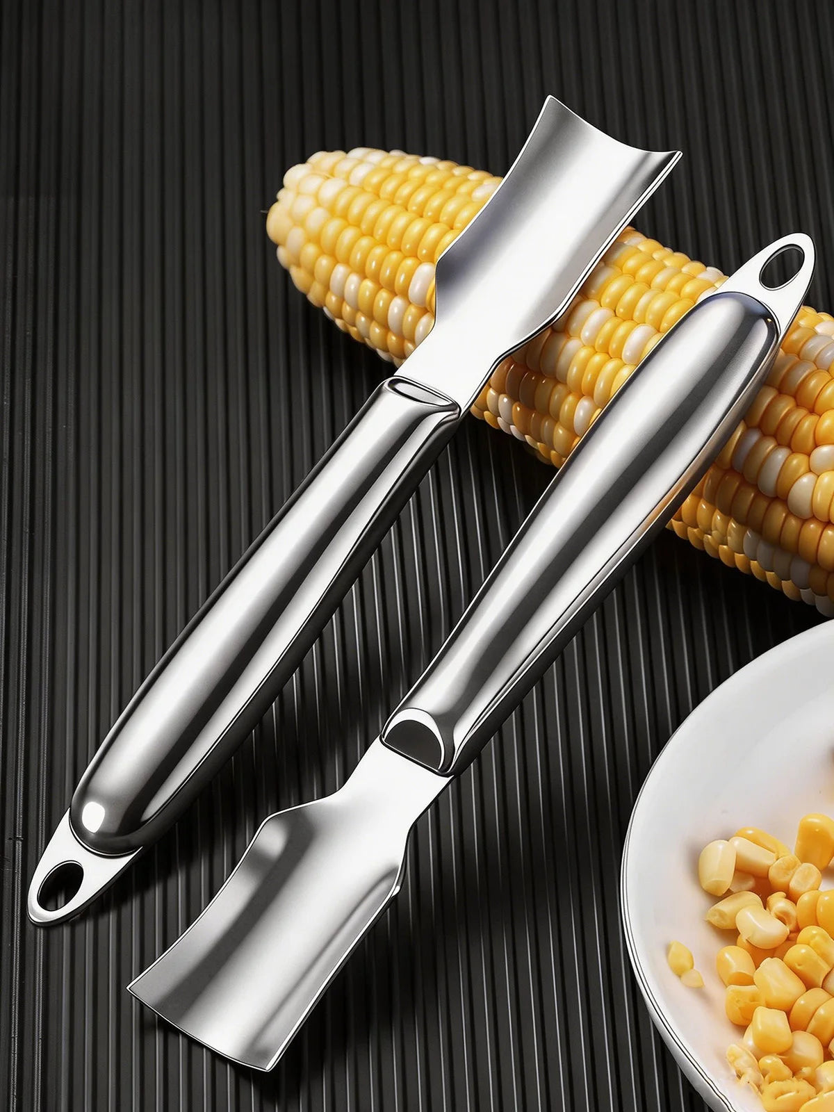 A stainless steel corn kernel remover peeler is shown against a dark background with corn kernels nearby.