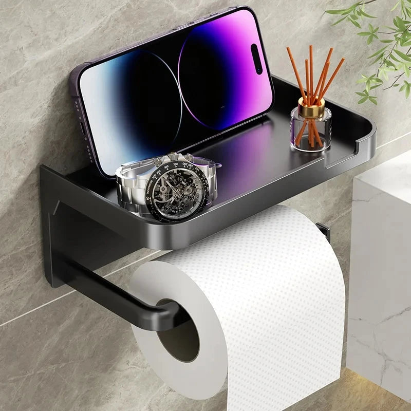 A black storage shelf mounted on a wall holds a smartwatch and a glass jar of wooden sticks above a roll of white toilet pape