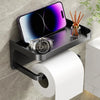 A black storage shelf mounted on a wall holds a smartwatch and a glass jar of wooden sticks above a roll of white toilet pape