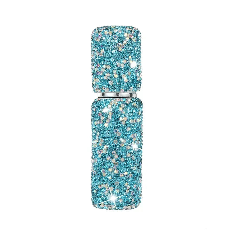 A clear glass perfume spray bottle filled with sparkling blue glitter and small rhinestones.