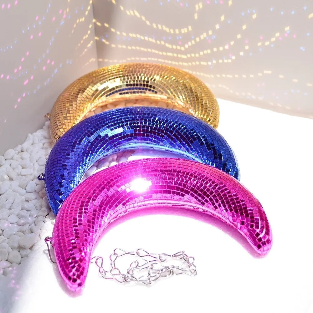 A display of three iridescent, curved moon-shaped pendants in gold, blue, and pink sequins.