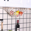 A woven sisal fruit hammock storage basket holding apples and lemons hanging on a kitchen cabinet rack.