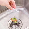 A hand is placing a clear disposable sink drain filter bag filled with vegetable scraps into a stainless steel kitchen sink d