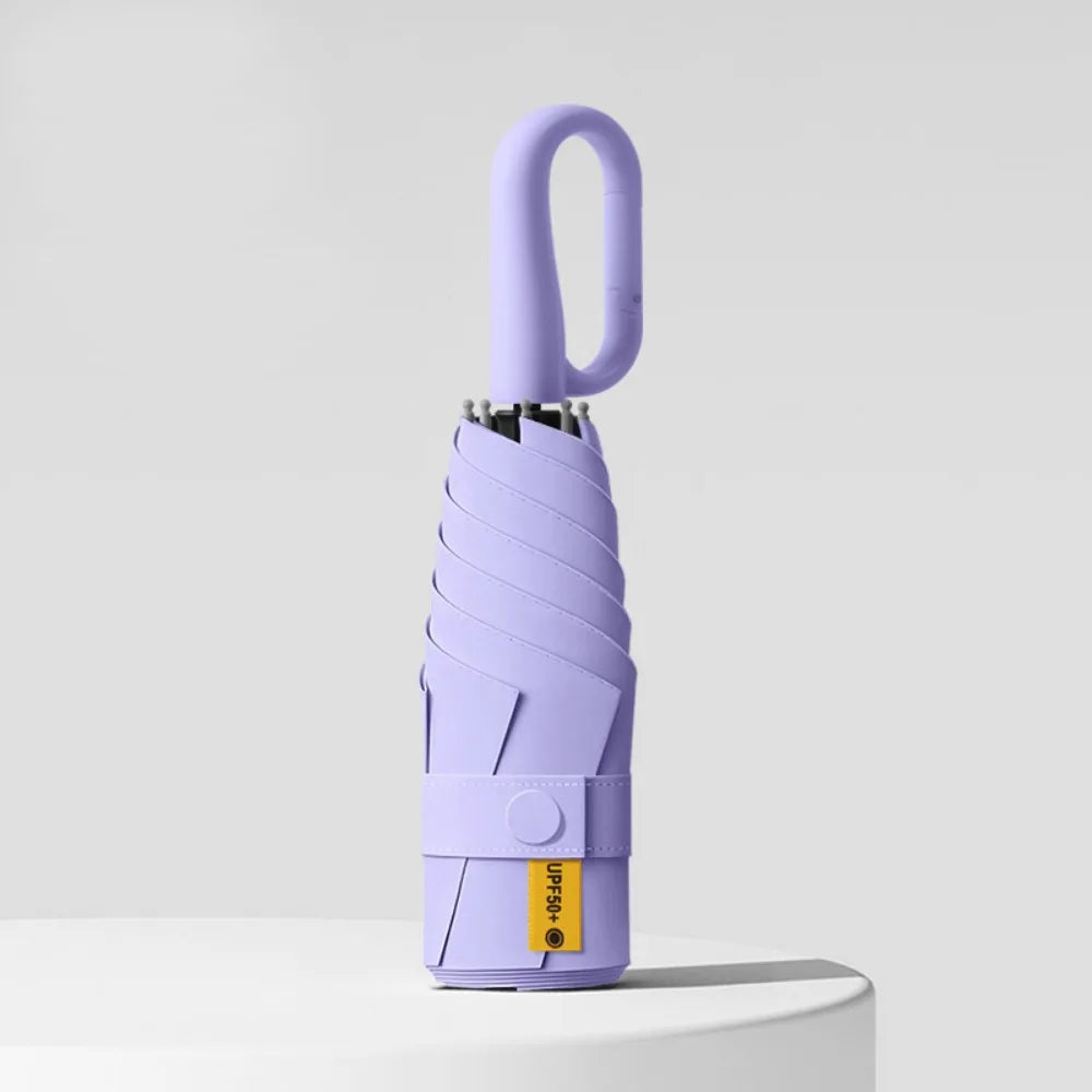 A purple compact folding umbrella with a handle is shown against a light gray background.