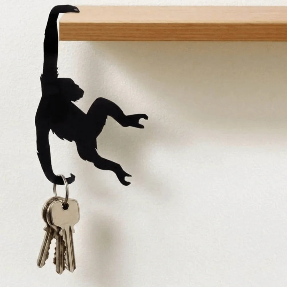 Black silhouette of a monkey figure with a key hanging from its hand on a white wall.