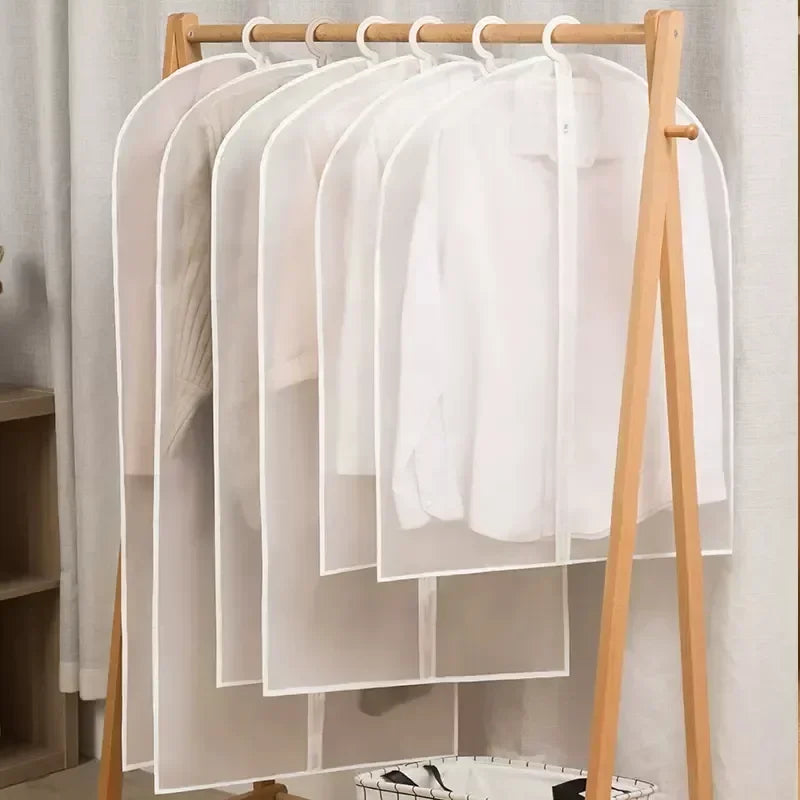 A wooden hanger displays several white washable clothes hanging with sheer dust covers.