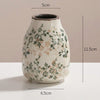 A ceramic bud vase with a speckled white glaze and green floral pattern, shown from the side.