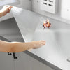 A hand is applying a self-adhesive aluminum foil kitchen wall sticker to a countertop, protecting it from oil and water.