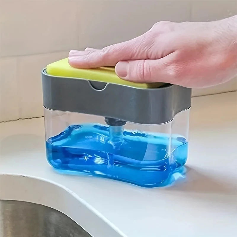 A hand is holding a clear liquid soap dispenser with a gray top and a yellow sponge holder, showing blue liquid inside.