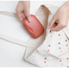 Hands place a terracotta-colored portable travel soap box into a light fabric pouch.