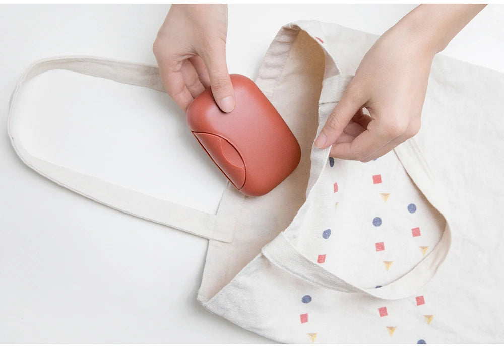 Hands place a terracotta-colored portable travel soap box into a light fabric pouch.