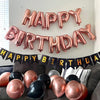 A decorative wall display of foil balloon letters spelling HAPPY BIRTHDAY in rose gold and pink tones.