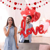 Junges Paar lächelt inmitten von roten und rosa herzförmigen Ballons für einen besonderen Anlass.