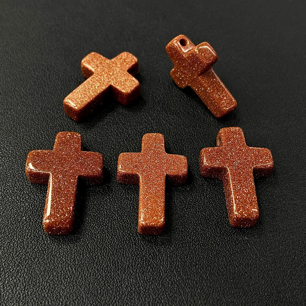 Five small, reddish-brown natural agate and jasper cross pendant charms arranged on a dark surface.