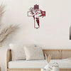 A piece of red metal wall art depicting a stylized face within a cross shape displayed above a wicker bed.