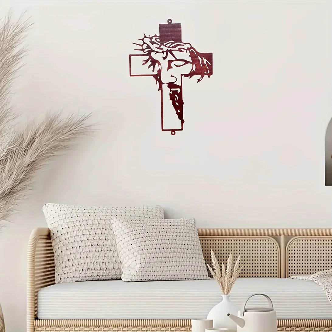 A piece of red metal wall art depicting a stylized face within a cross shape displayed above a wicker bed.